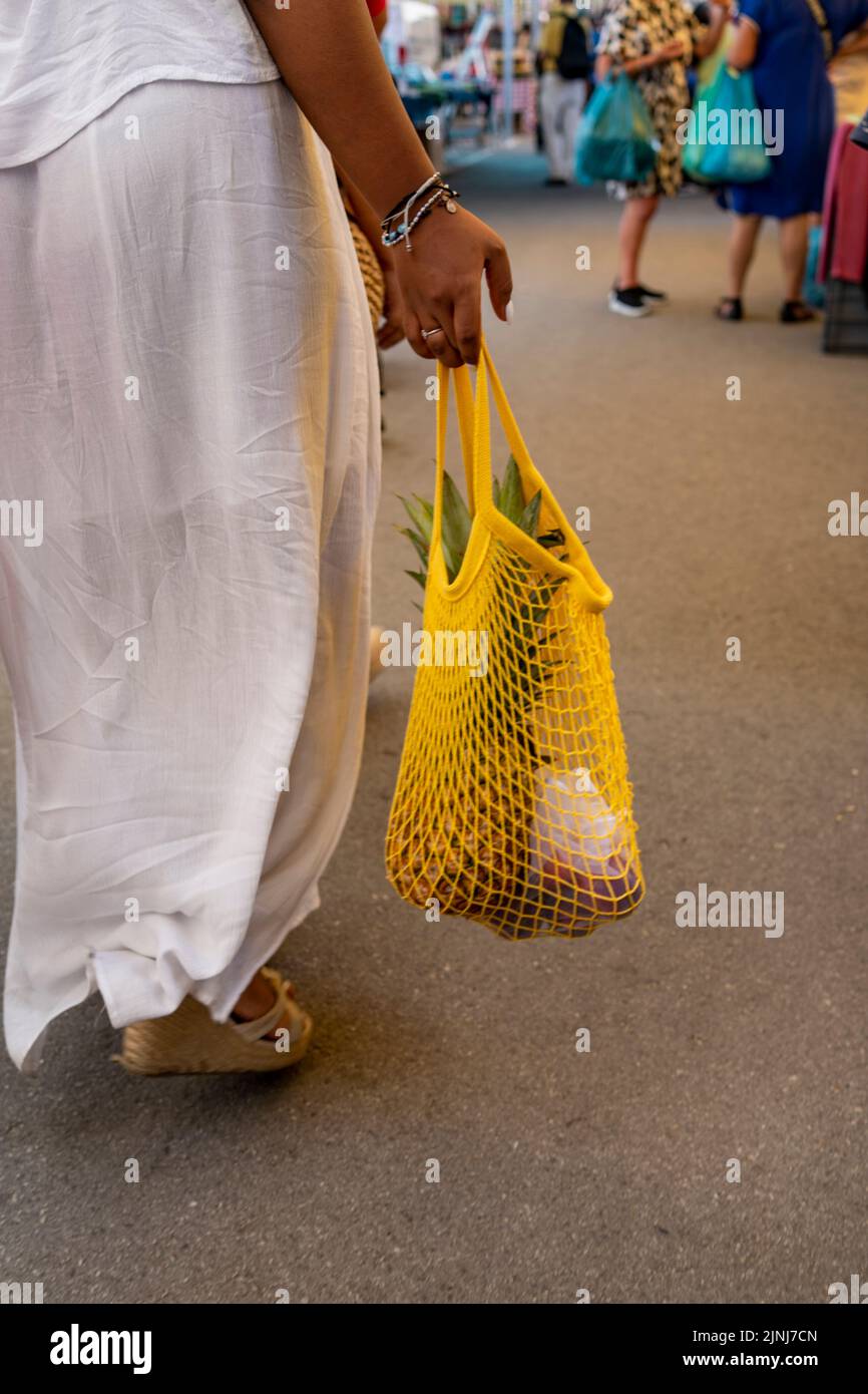 Woman in white dress with shopping in reusable cotton net bag at local market, zero waste concept. Stock Photo