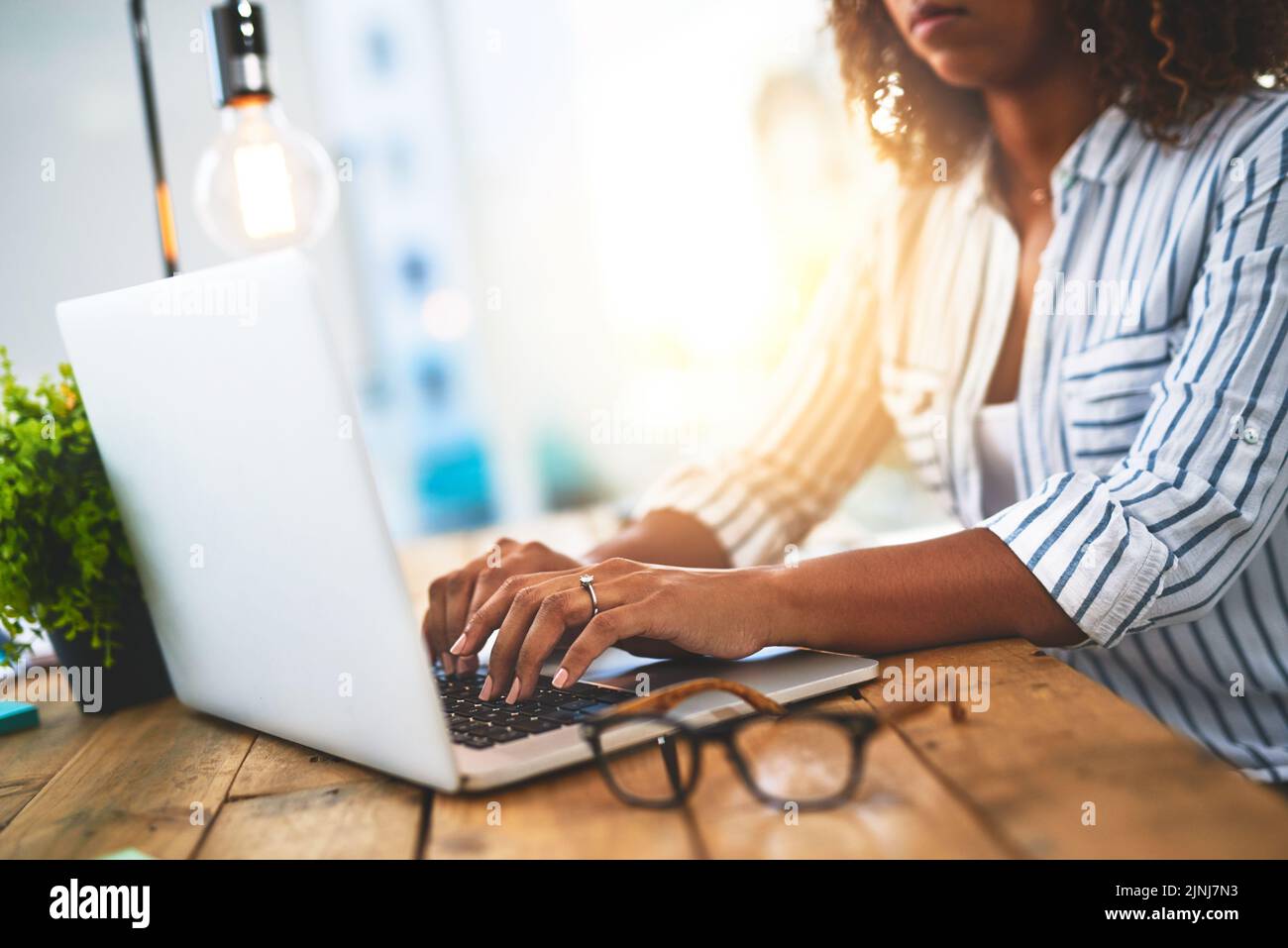 Hands of a woman working with her laptop on a wooden table indoors. Closeup of entrepreneur typing in an open plan home office. Female blog writer Stock Photo