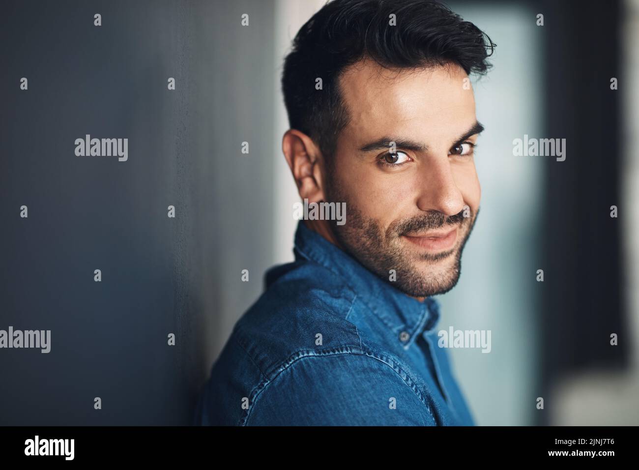Portrait of confident and casual man leaning against a grey wall looking happy, proud and glad while smiling. Face of stylish, handsome and young Stock Photo