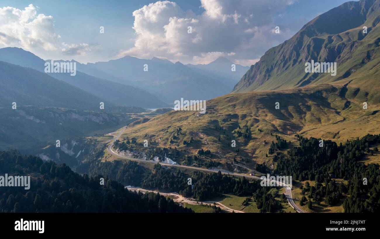Aerial view towards the Lukmanier Pass, a mountain pass in the Swiss Alps in the canton of Graubunden. A rocky ridge on the right leads the eye towards the road that flows sinuously in the valley.  Stock Photo
