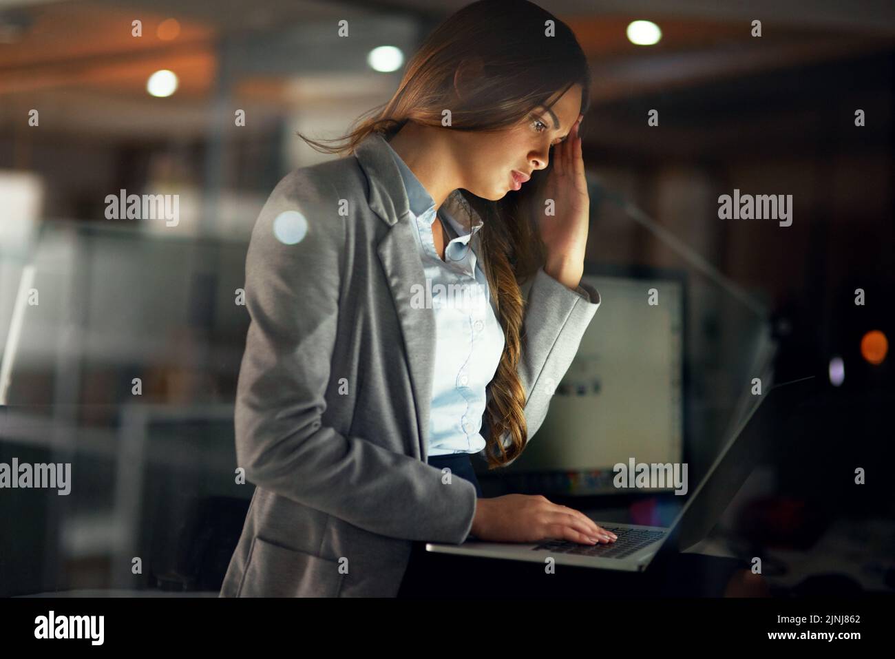 Stressed, worried and tired female entrepreneur typing on a laptop and working overtime late at night. Frustrated and overworked young businesswoman Stock Photo