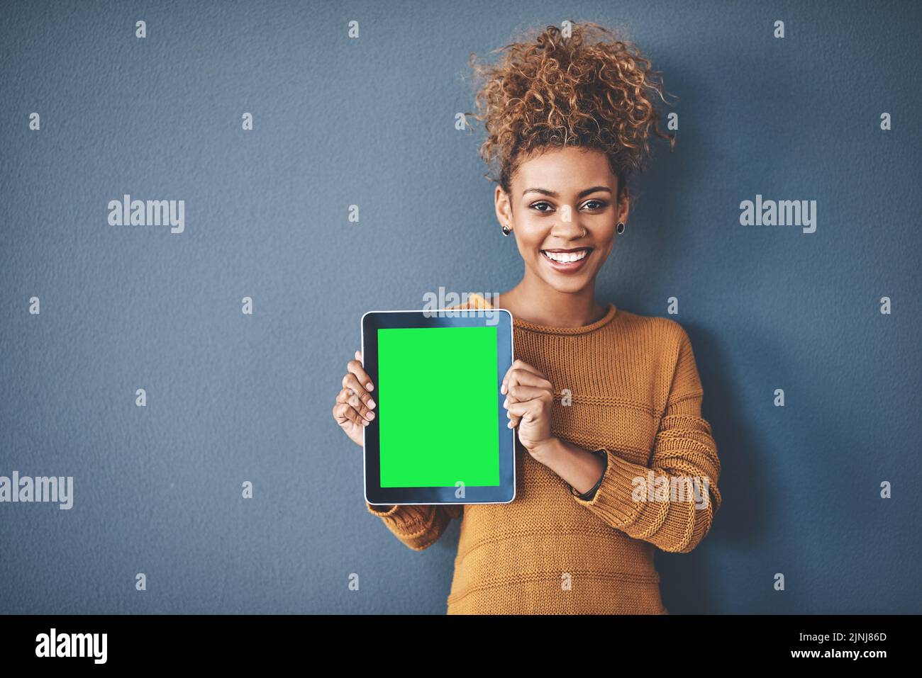 African female holding green screen tablet copyspace. Cute, attractive and smiling young afro woman standing and showing a mobile device.Happy Stock Photo