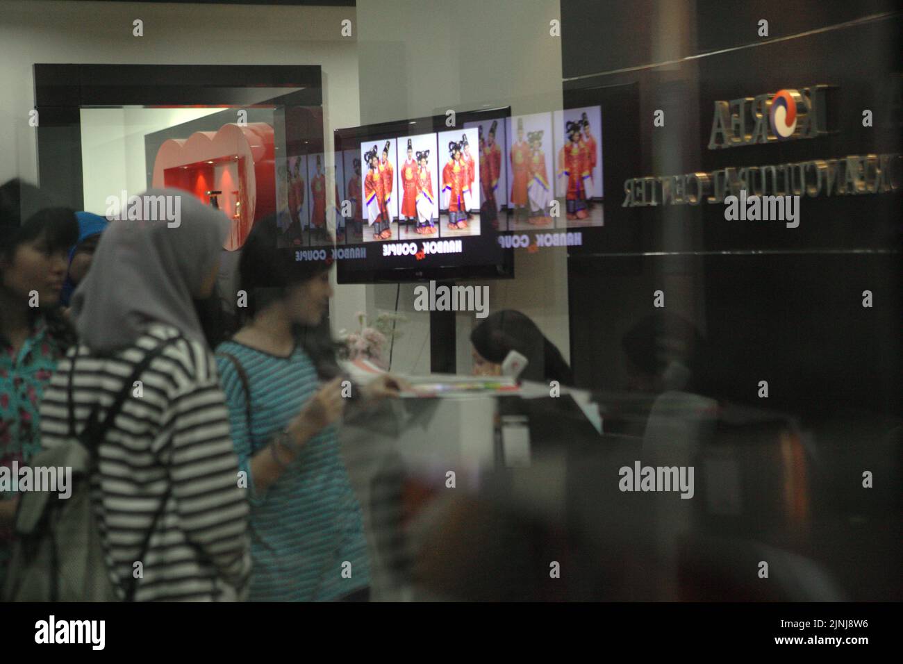 A group of students are photographed from behind a glass wall as they are standing and walking in front of the front desk of Korean Cultural Center (KCC) in Jakarta, Indonesia. Stock Photo