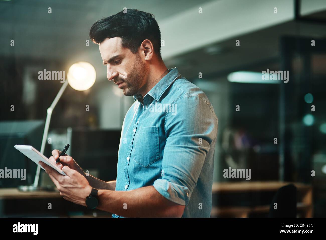 Serious design business architect thinking and working on his tablet in a modern casual office at night. Professional designer drawing and planning Stock Photo