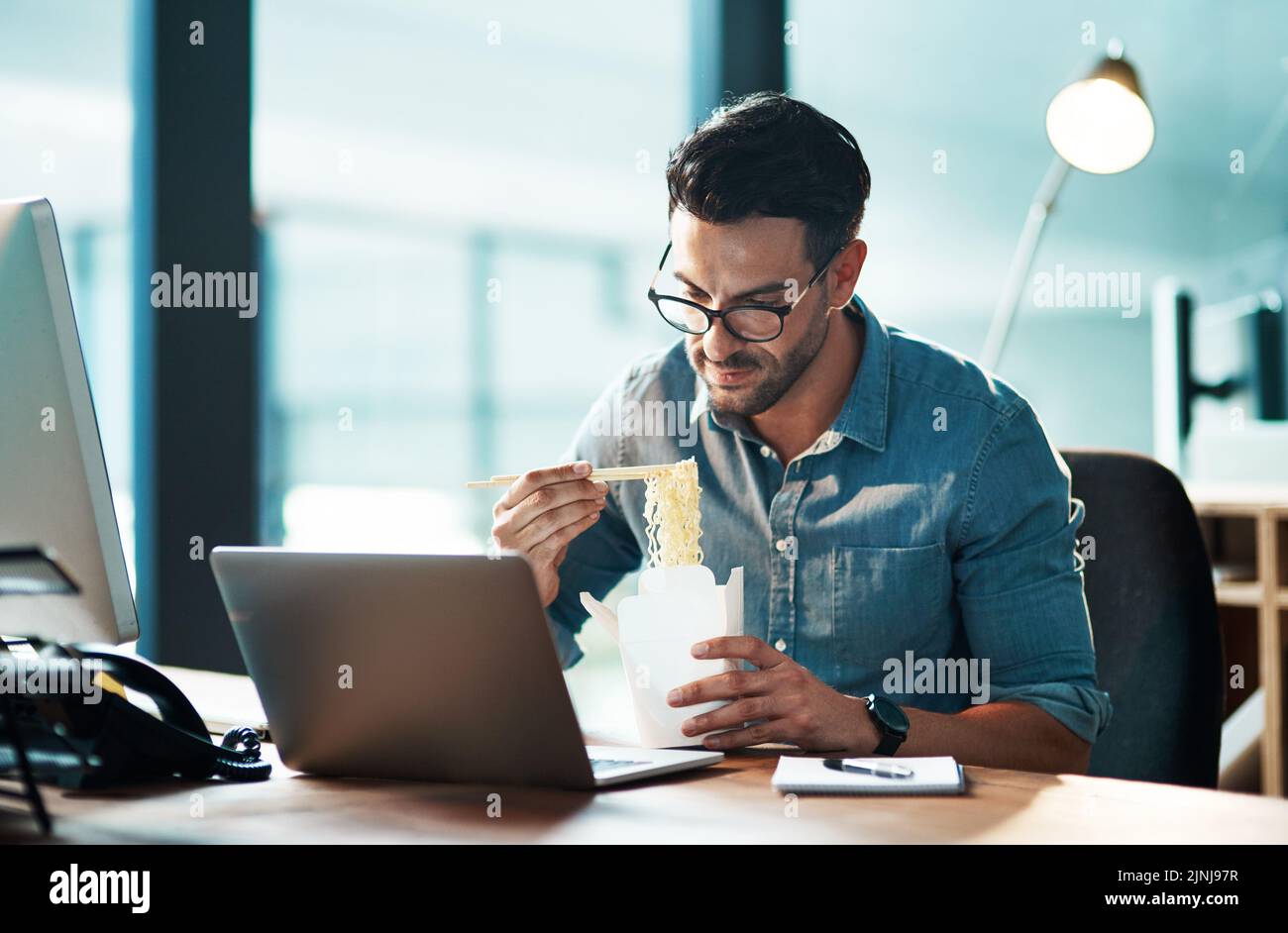 Business man eating lunch at his desk, reading an email on a laptop and working overtime in office. Corporate professional, manager or employee Stock Photo