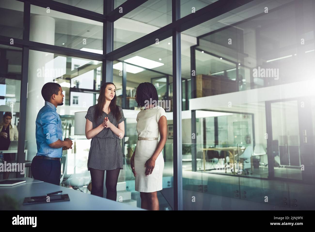 Business team standing and talking inside of the office together. Meeting and open discussion with colleagues in the workplace. Corporate mentor Stock Photo
