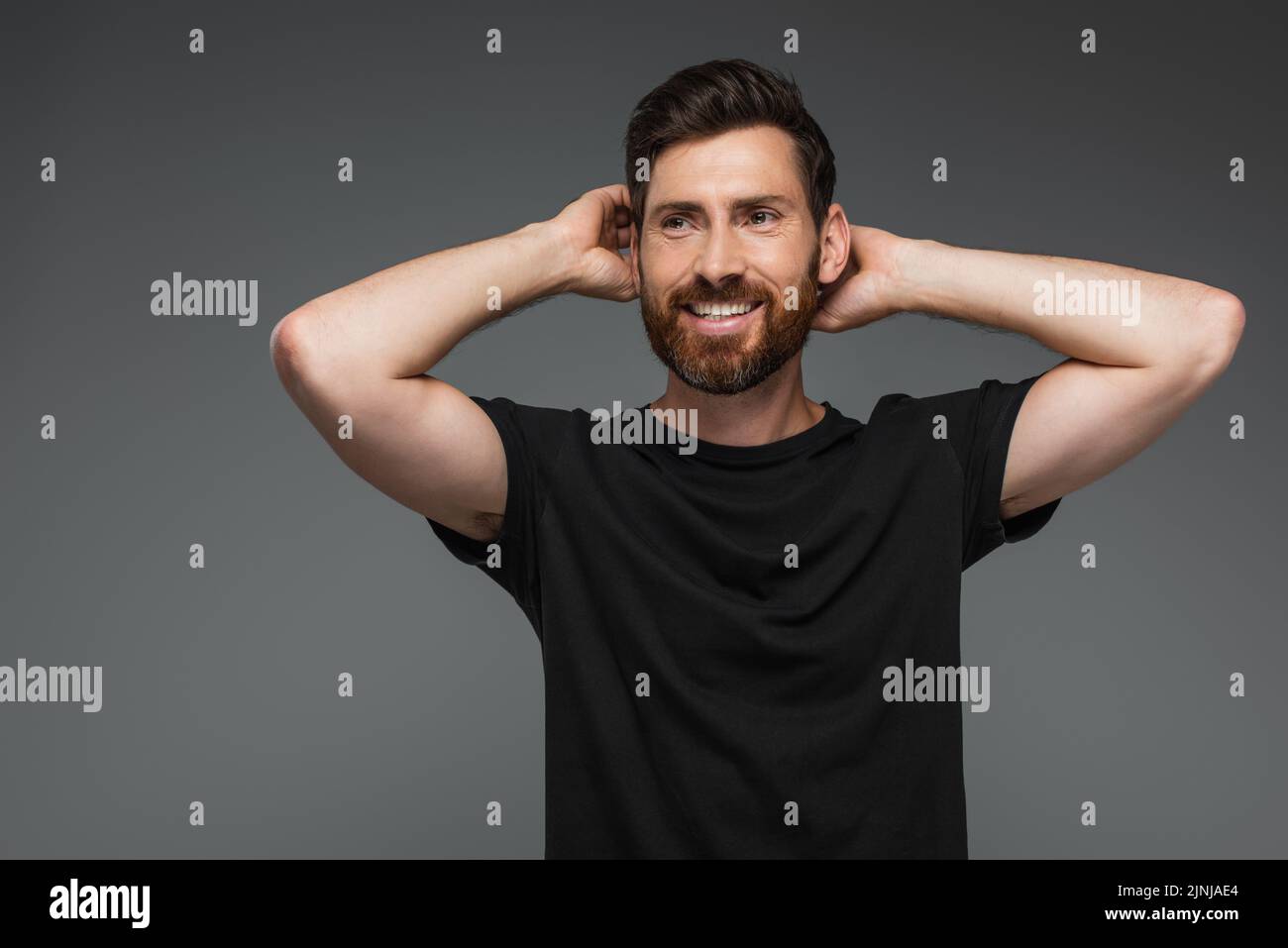 portrait of cheerful man in black t-shirt posing with hands behind head isolated on grey,stock image Stock Photo