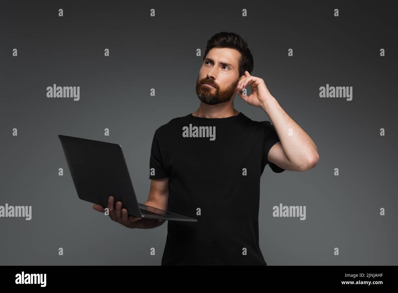 pensive freelancer with beard holding laptop and looking away isolated on grey,stock image Stock Photo