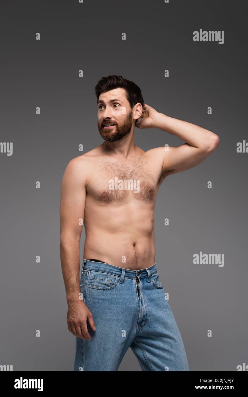 puzzled and shirtless man with beard standing in denim jeans isolated on grey,stock image Stock Photo
