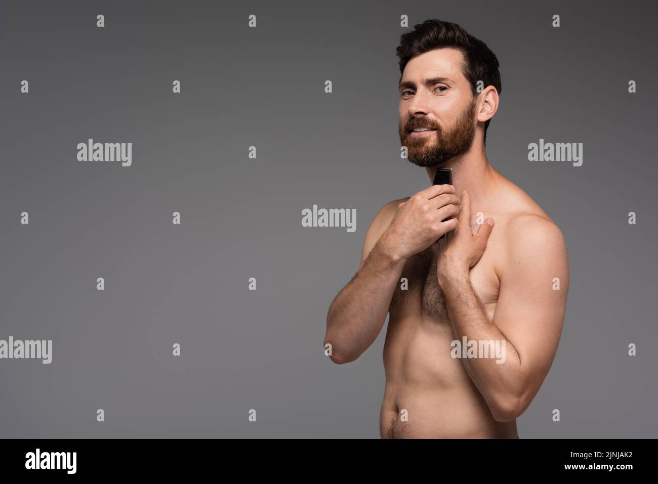 bearded and shirtless man shaving with electric razor isolated on grey,stock image Stock Photo