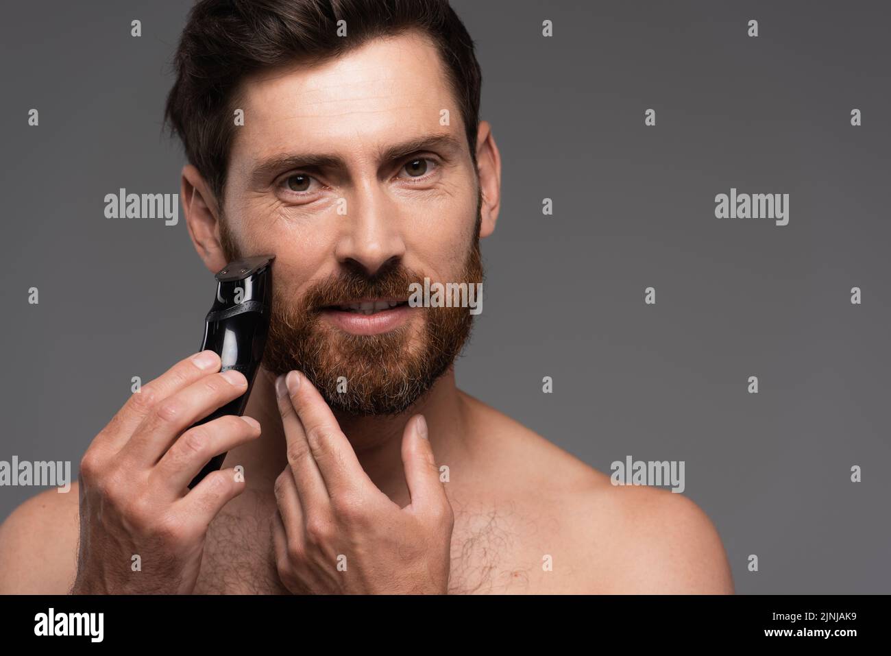shirtless man with hair on chest shaving beard with electric razor isolated on grey,stock image Stock Photo