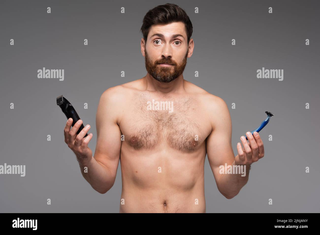 confused and shirtless man with beard holding safety and electric razors isolated on grey,stock image Stock Photo