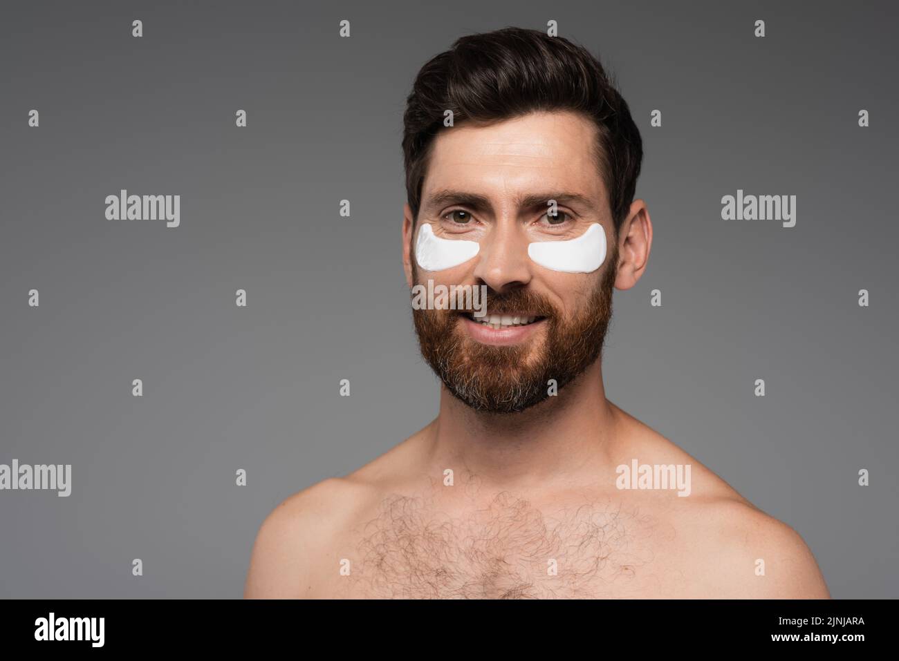 happy bearded man with moisturizing eye patches isolated on grey,stock image Stock Photo
