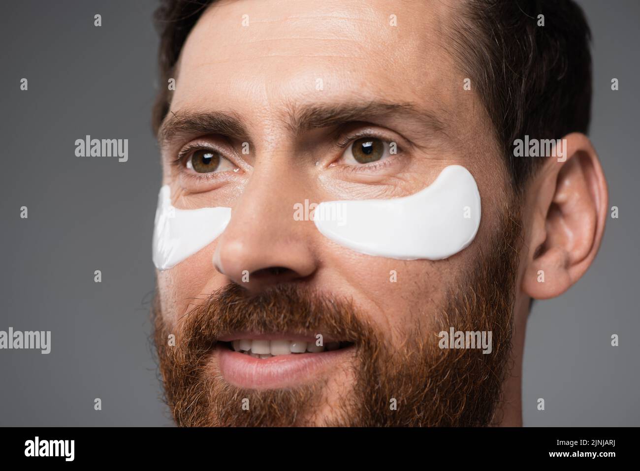 close up view of cheerful bearded man with moisturizing eye patches isolated on grey,stock image Stock Photo