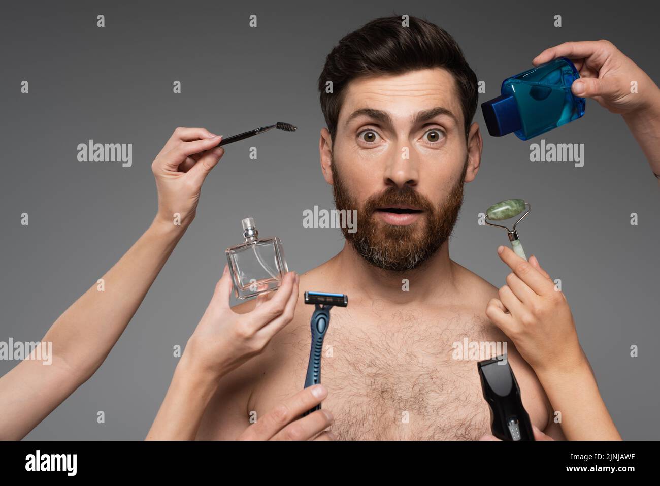women holding beauty products around bearded and surprised man on grey,stock image Stock Photo