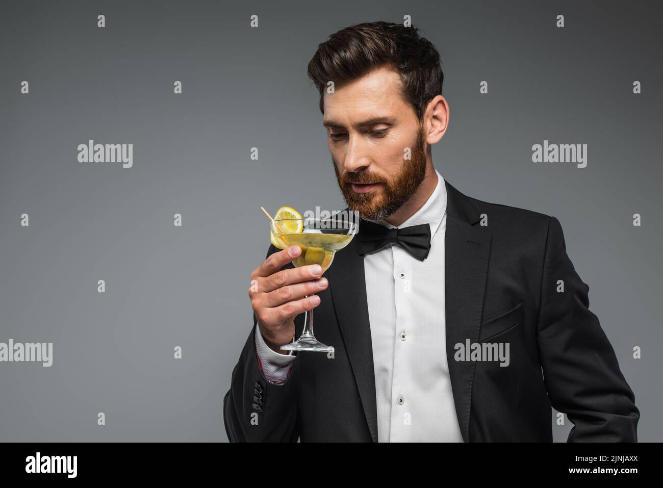 bearded man in suit looking at glass with cocktail isolated on grey,stock image Stock Photo