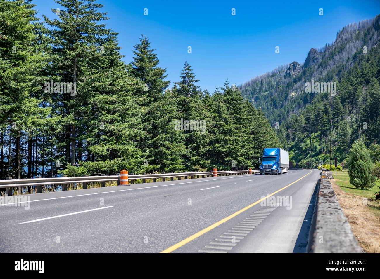 Blue industrial big rig semi truck with truck driver cab sleep compartment transporting cargo in dry van semi trailer running on summer highway road w Stock Photo