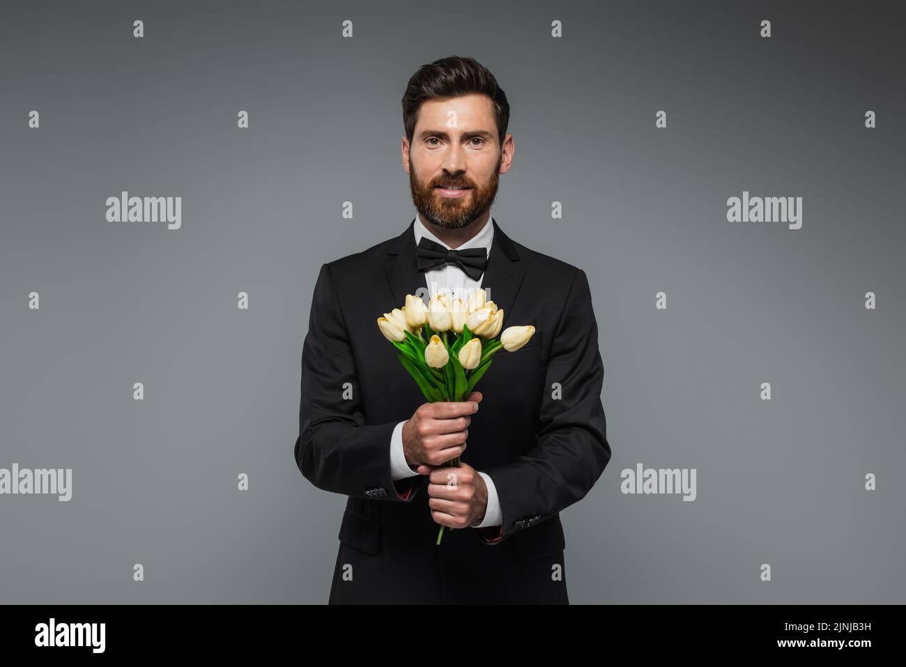 bearded man in elegant suit with bow tie holding bouquet of tulips isolated on grey,stock image Stock Photo