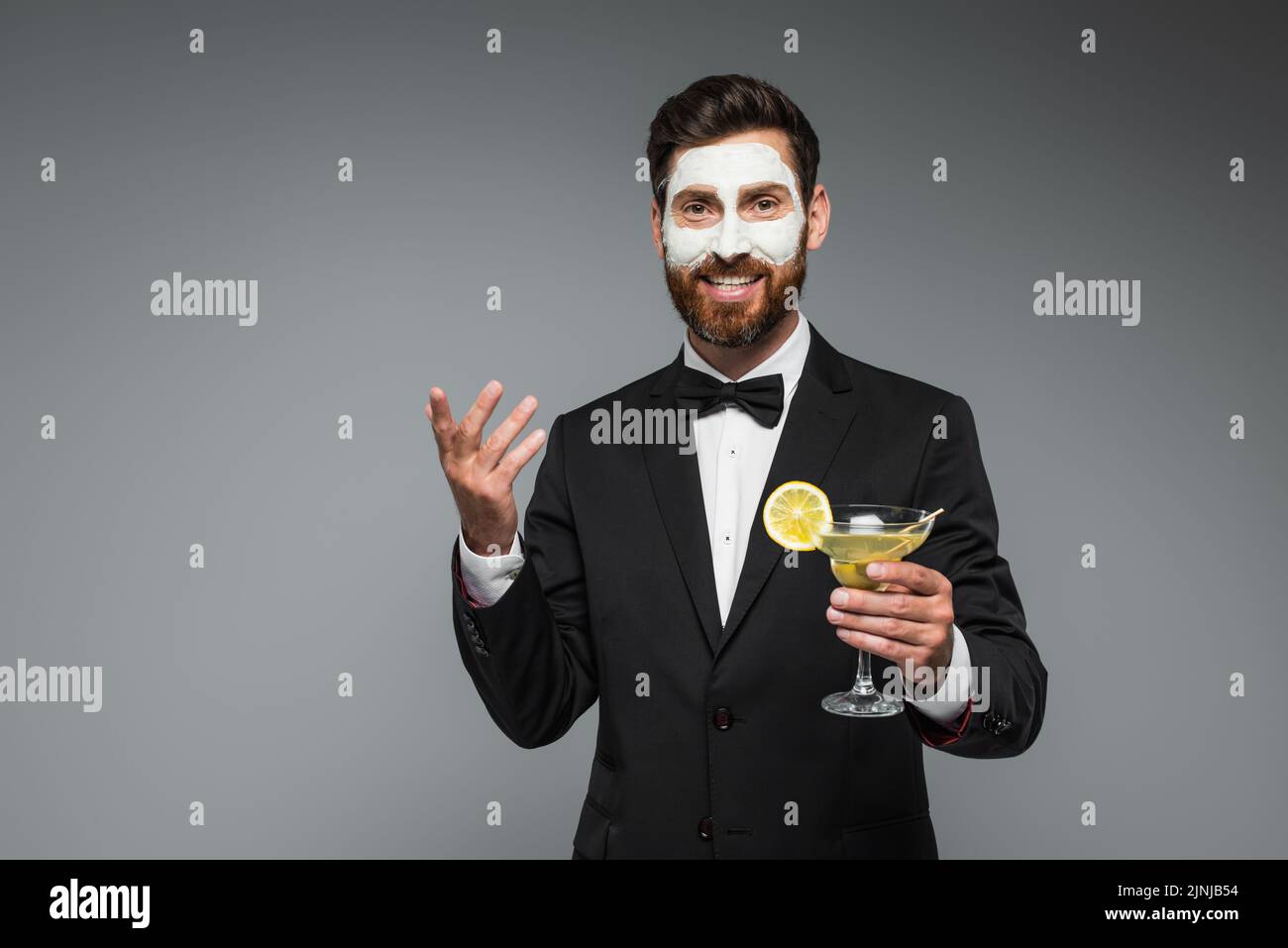 joyful bearded man in suit with clay mask on face holding cocktail isolated on grey,stock image Stock Photo