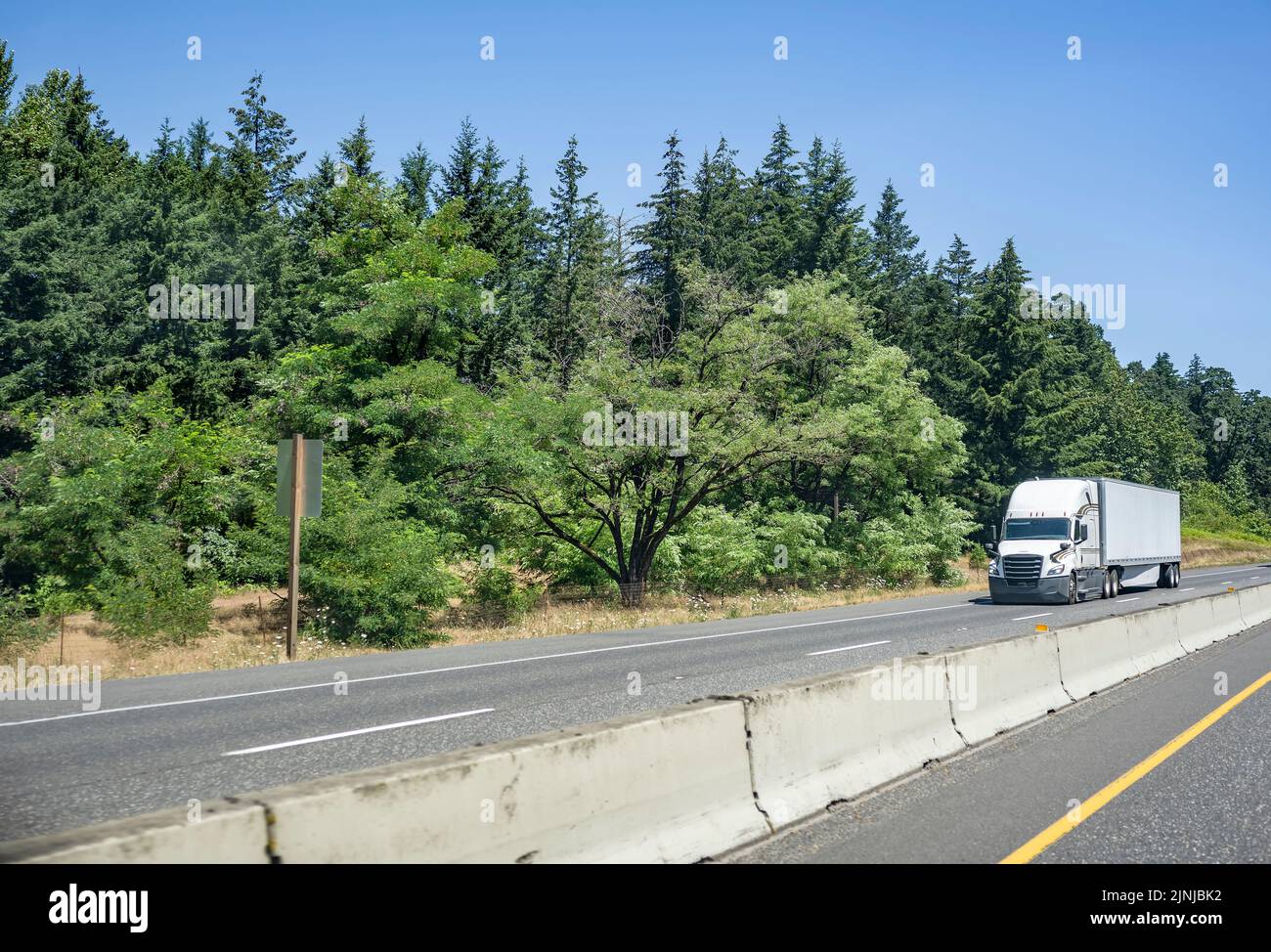 Industrial grade white big rig semi truck tractor with high roof and sleeping compartment transporting commercial cargo in dry van semi trailer runnin Stock Photo
