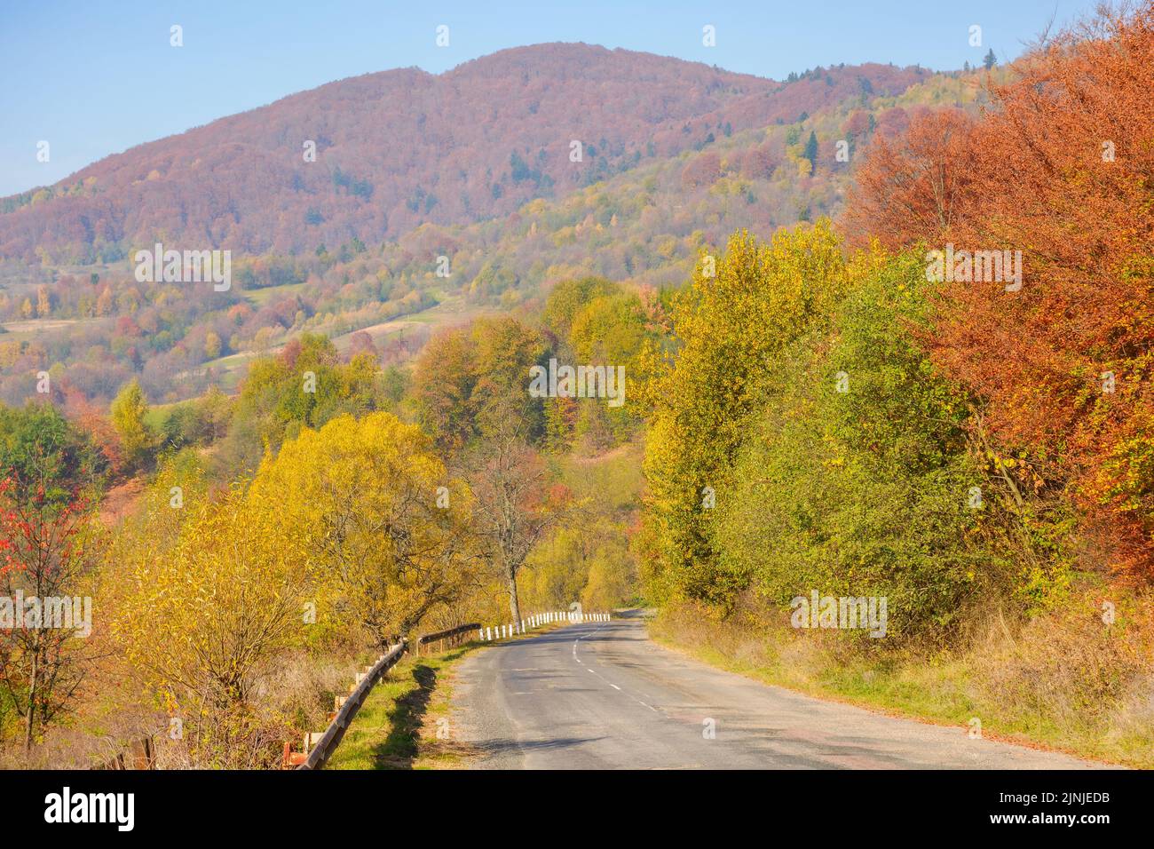 old asphalt rural serpentine in mountains. countryside tourism on a sunny autumn morning. forested hills in colorful foliage. blue sky with fluffy clo Stock Photo