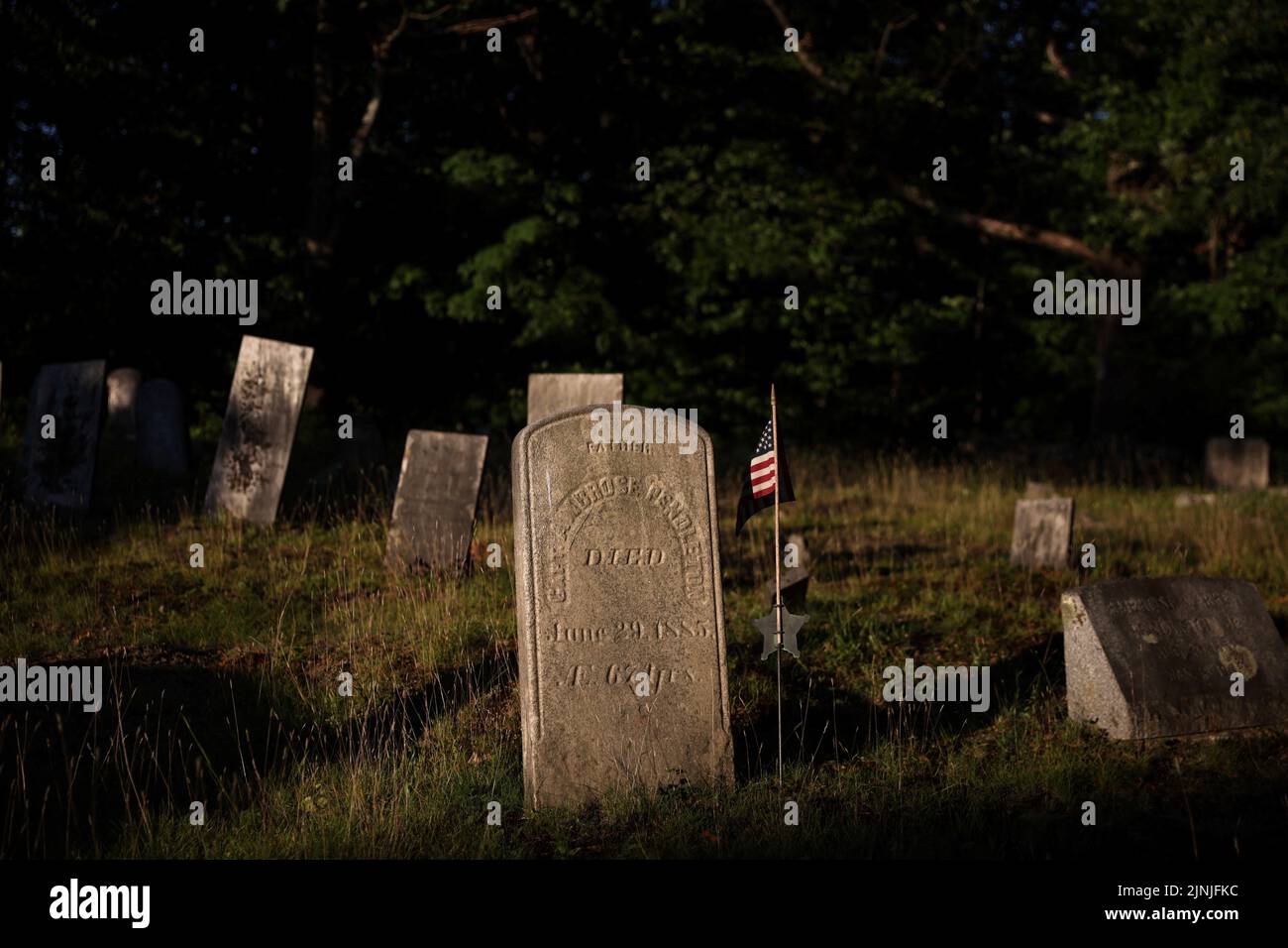 A tombstone sits with a U.S. flag at a cemetery near Corinth, New York, U.S., July 21, 2022. REUTERS/Shannon Stapleton Stock Photo