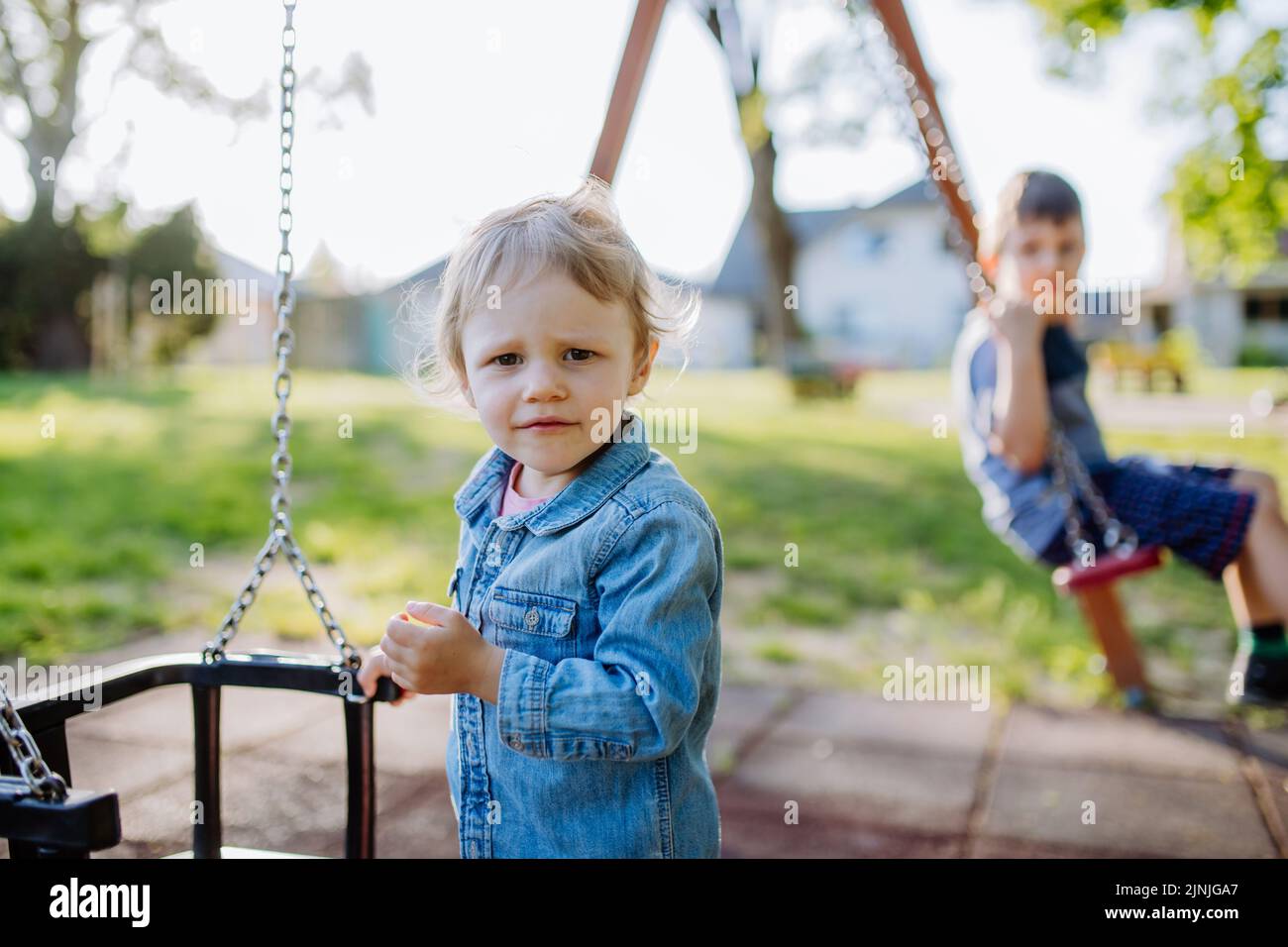 Little sibling playing together in playground, swaying on a swing