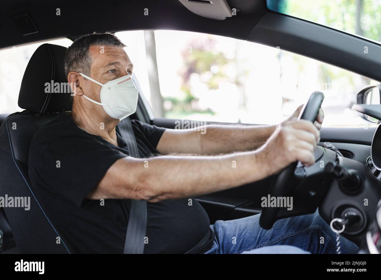 Senior in his 70s driving a car wearing face mask for protection against corona virus Stock Photo