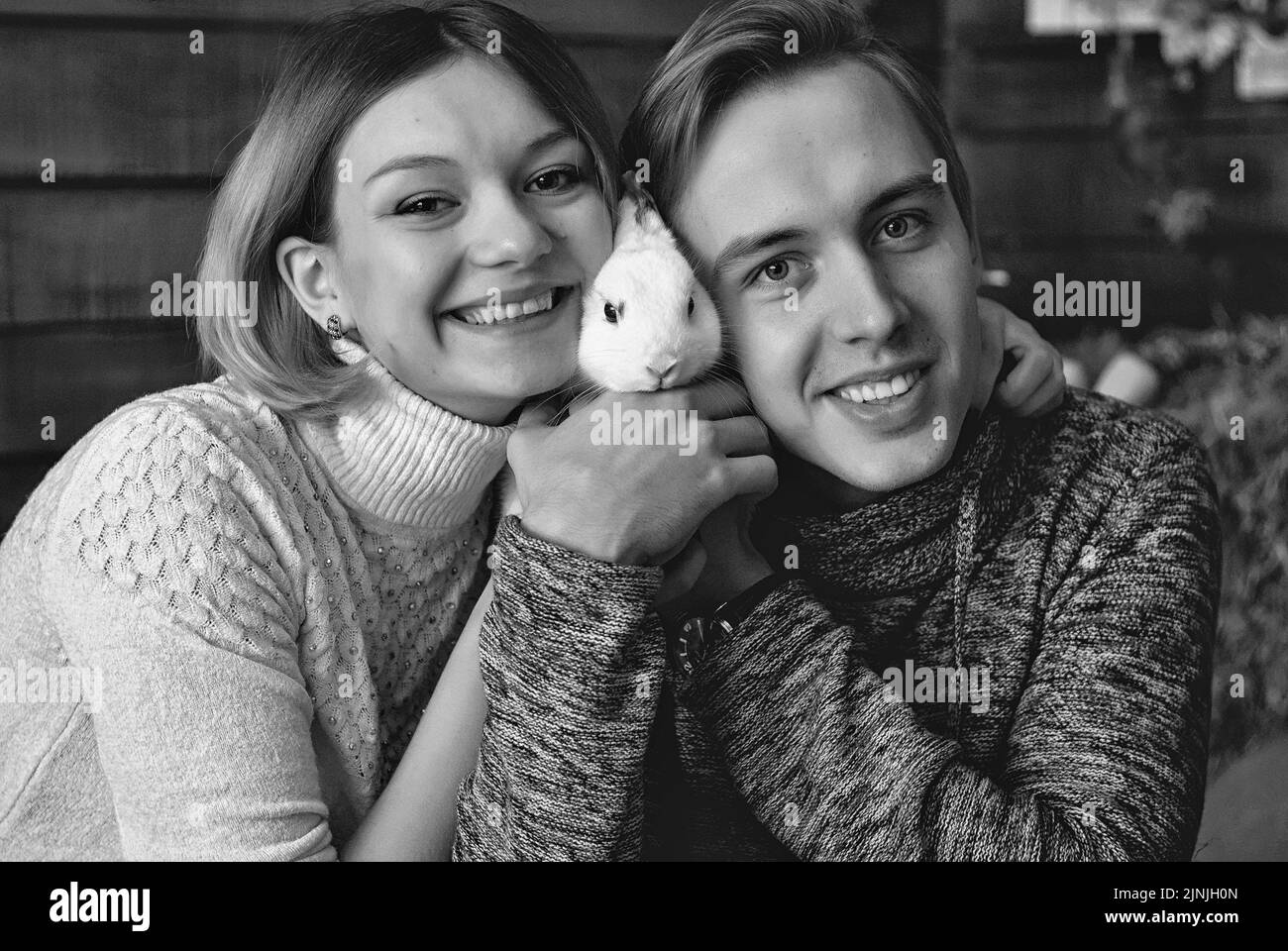 Love story of young happy, funny couple in studio, cozy home. White rabbit. Autumn decorations, orange pumpkins, leaves. Family holiday Stock Photo