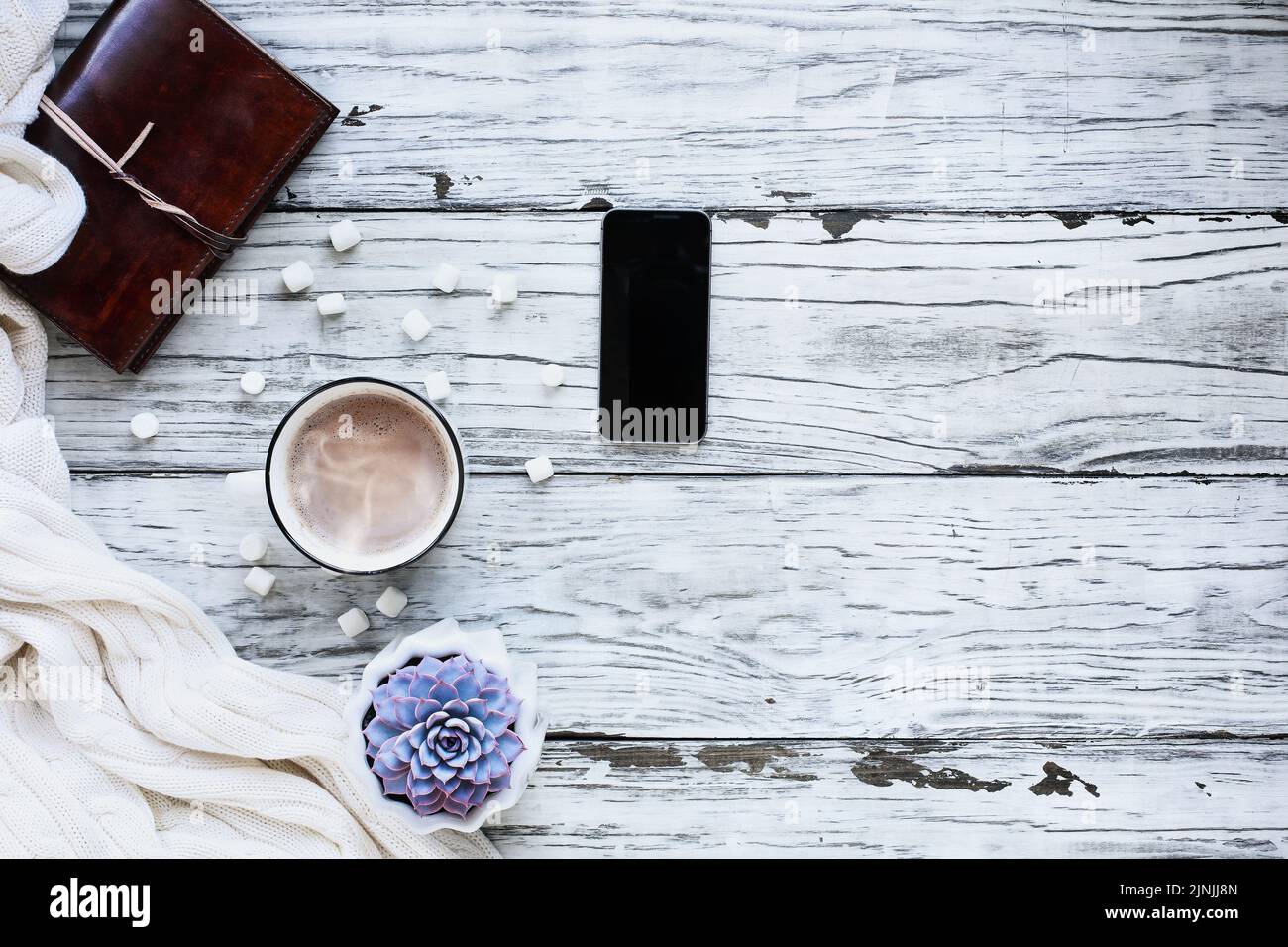 Autumn or winter background shot from top view with hot cocoa, houseplant, cell phone, book, and throw blanket over rustic white wood table. Stock Photo