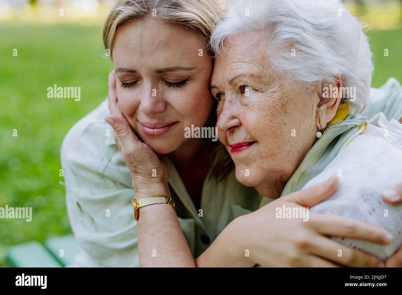 Worried senior grandmother comforting grown up granddaughter when sitting on bench in park, share problem with someone close concept Stock Photo