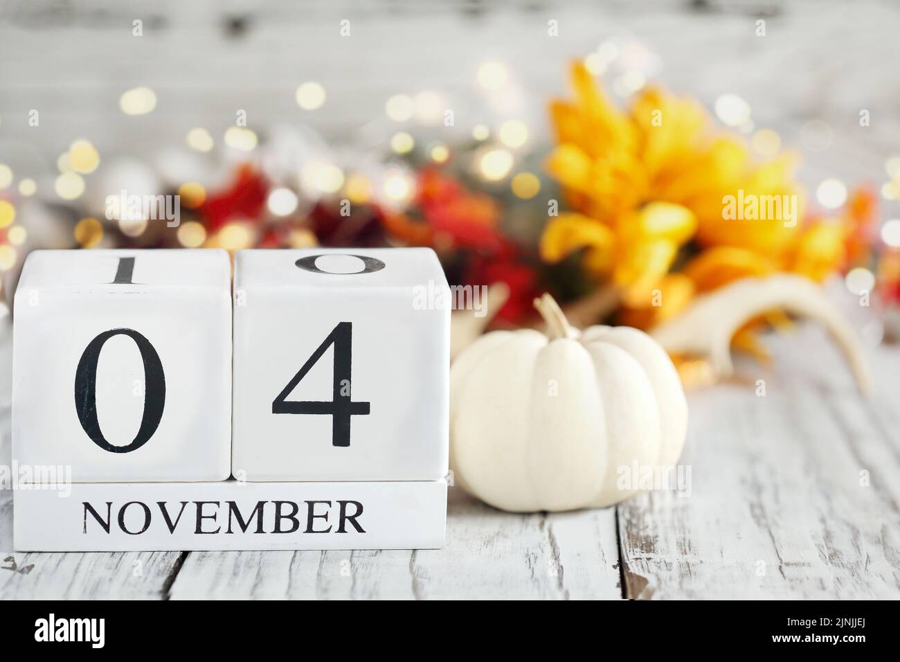 White wood calendar blocks with the date November 4th and autumn decorations over a wooden table. Selective focus with blurred background. Stock Photo