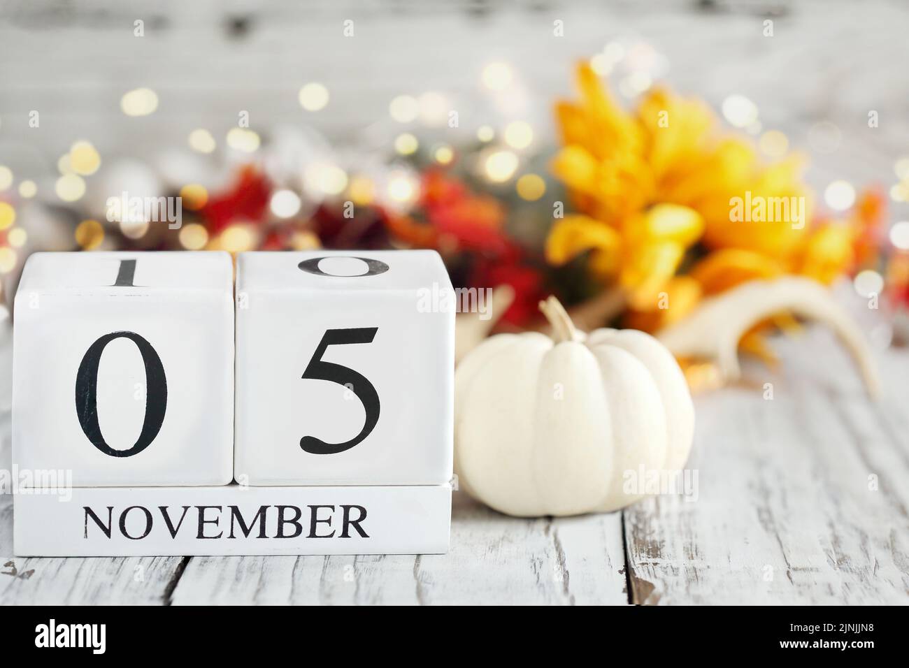 White wood calendar blocks with the date November 5th and autumn decorations over a wooden table. Selective focus with blurred background. Stock Photo