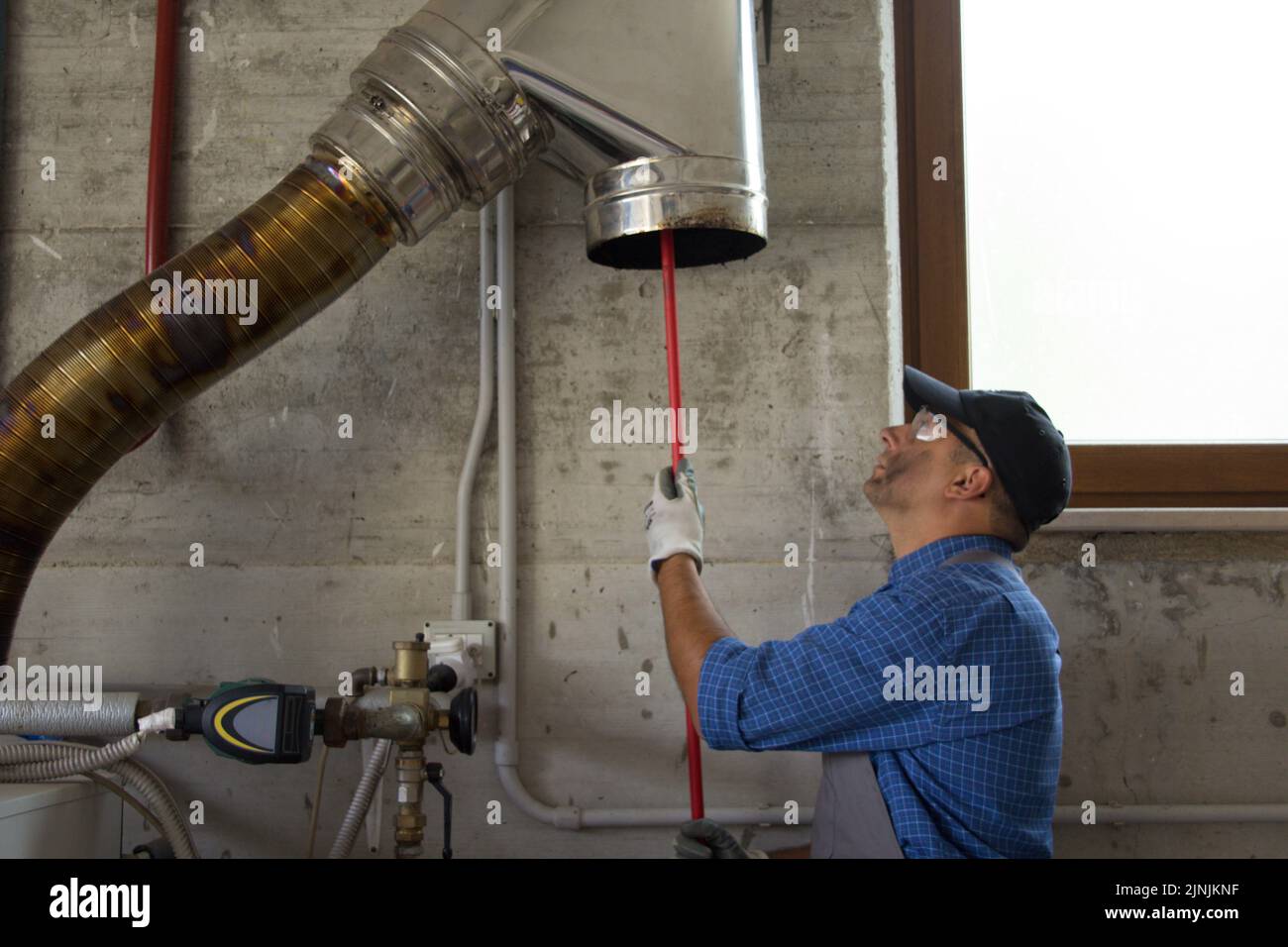 Picture of a handyman cleaning the stainless steel pipe of a boiler flue with a brush. I work as a chimney sweep Stock Photo