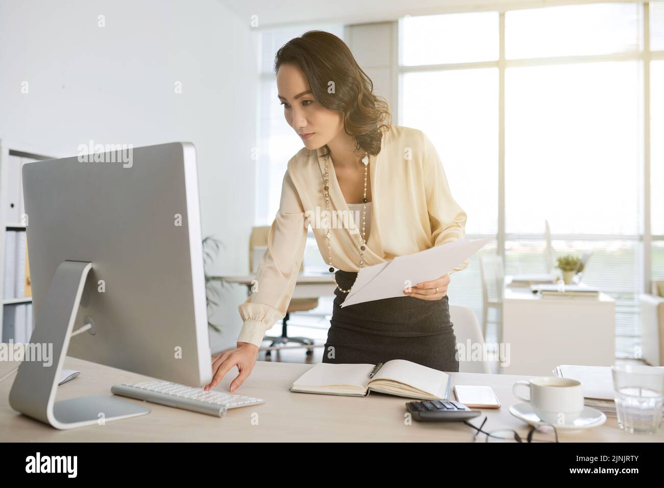 Asian business woman with documents checking her computer Stock Photo
