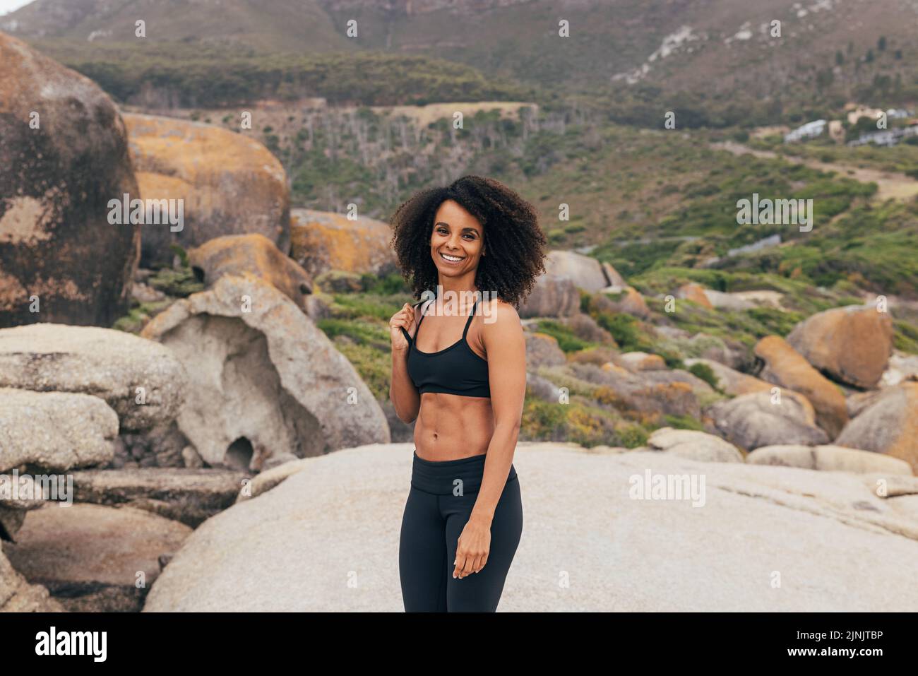 Beautiful woman with yoga mat standing outdoors. Smiling female in sportswear relaxing after yoga exercises. Stock Photo