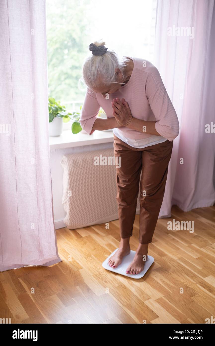 Senior worried woman stepping on floor scales, closeup. Weight control Stock Photo