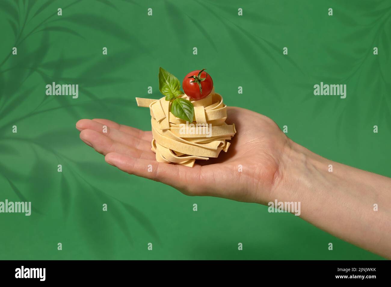 Pasta Tagliatelle Nest in Hand isolated on a Green background Stock Photo