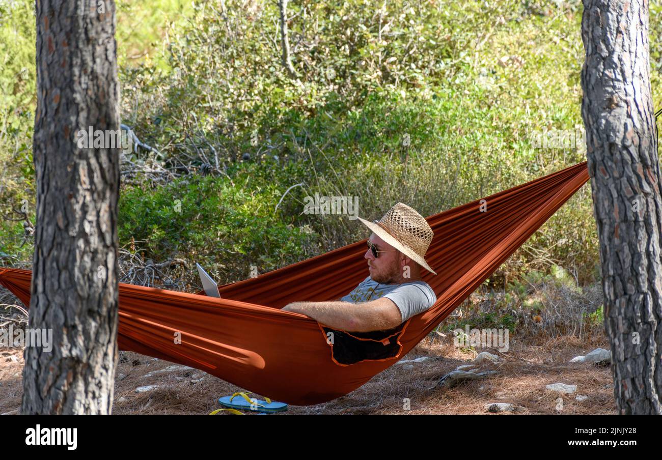 A view of a man relaxing in a hammock, using laptop computer Stock Photo