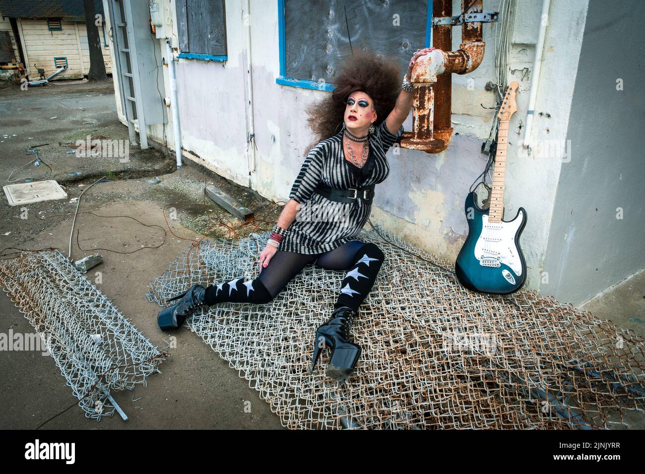 drag queen with big wig lying at abandoned building with a guitar Stock Photo