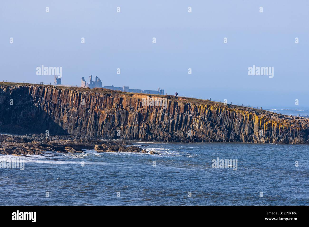 The Igneous rocks of Cullernose Point on the Northumberland Coast Path with Dunstanburgh Castle in the background, Northumberland, England Stock Photo