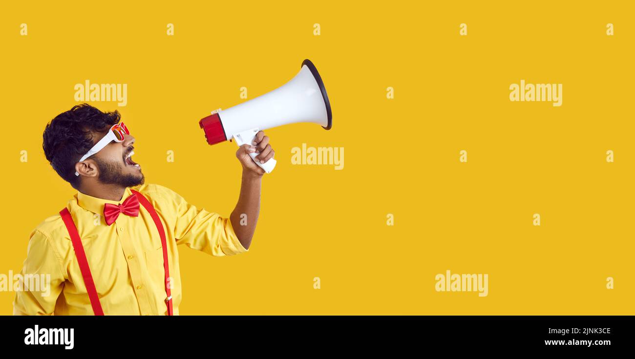 Funny guy with megaphone making announcement on yellow copy space banner background Stock Photo