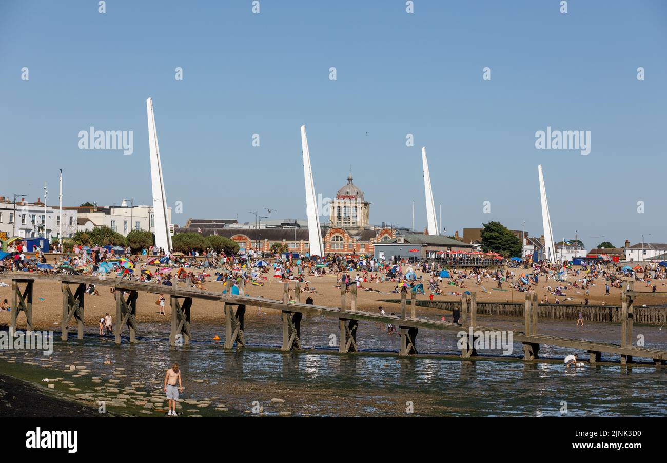 Crowds of tourists pack the beach at low tide on a hot sunny day, with the Kursaal building and Southend beach skyline in the background Stock Photo