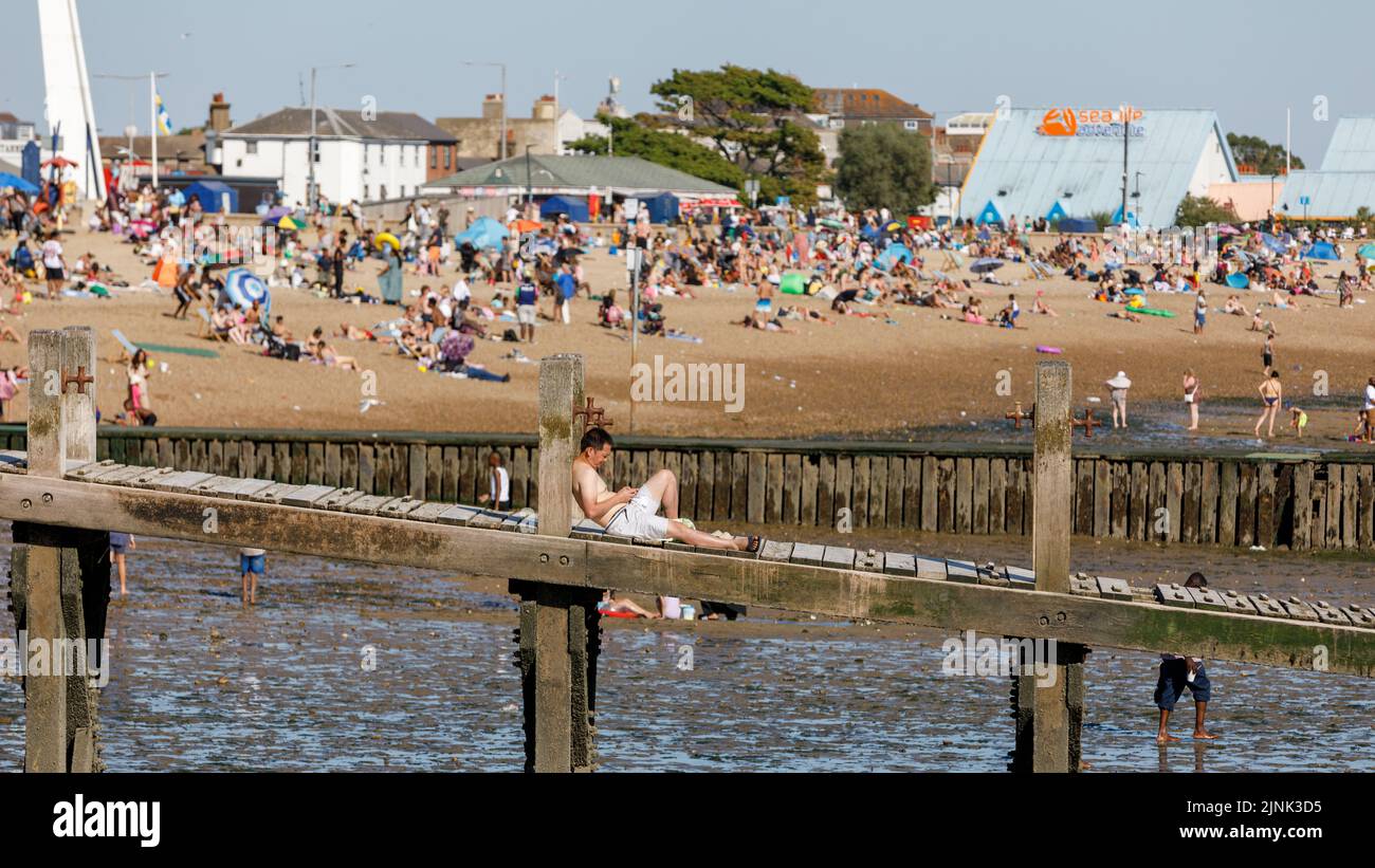 A teenager relaxes on a jetty on a beach full of people on a hot sunny day. Summer, packed, multicultural. UK heatwave Stock Photo