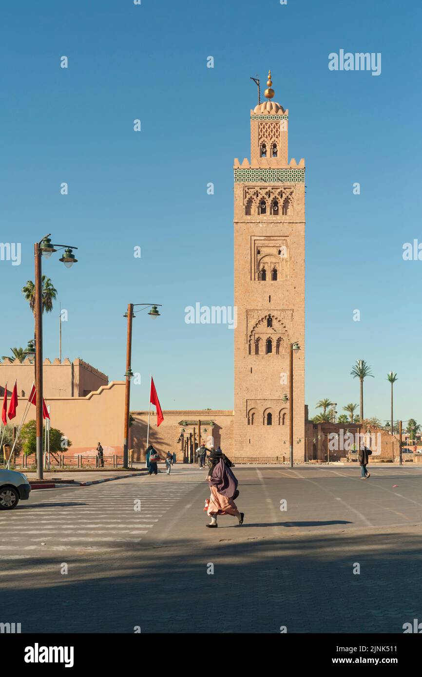 Veiled muslim woman passing by the minaret of Koutoubia Mosque, Marrakesh, Morocco Stock Photo