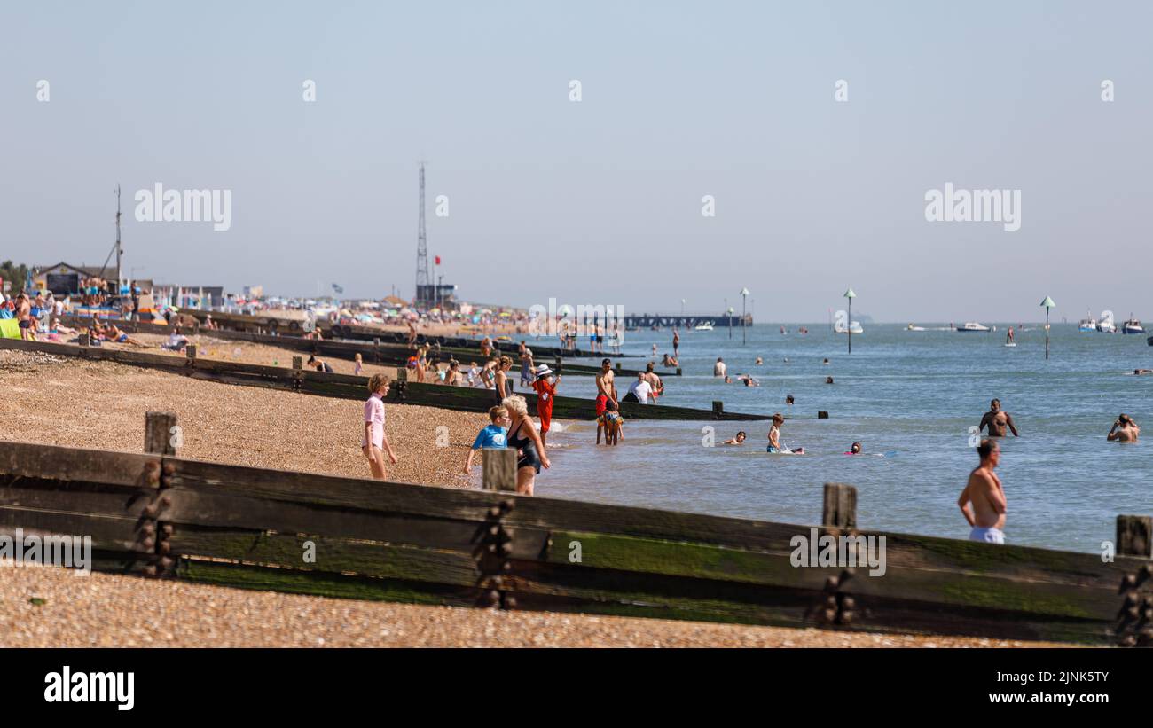 People walk on the beach and paddle in the sea during the summer heatwave in England Stock Photo