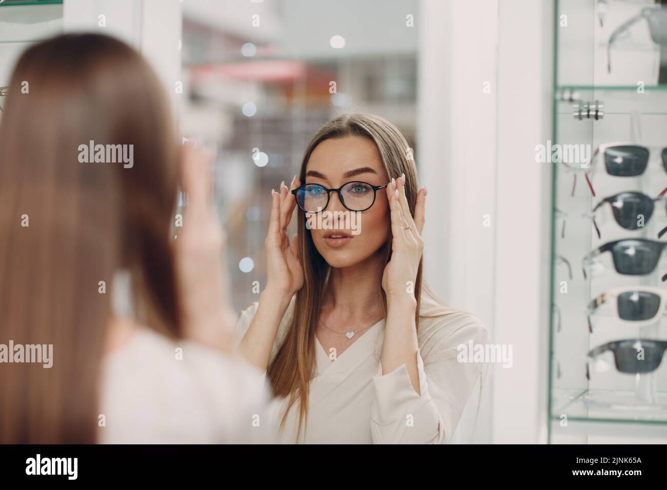 Young woman wearing and choose glasses at optician corner at shopping