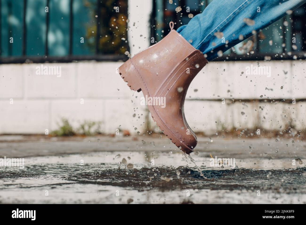Woman wearing rain rubber boots walking running and jumping into puddle ...