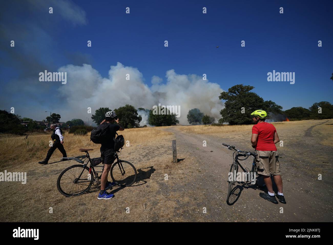 Cyclists take photos near the scene of a grass fire on Leyton flats in east London, as a drought has been declared for parts of England following the driest summer for 50 years. Picture date: Friday August 12, 2022. Stock Photo
