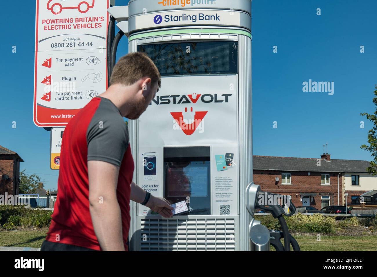 Young man using an electric vehicle chargepoint operated by Instavolt, a company owning a nationwide network of electric vehicle chargepoints, They announced price increases to 66p per kwh due to energy price crisis in summer 2022. Stock Photo